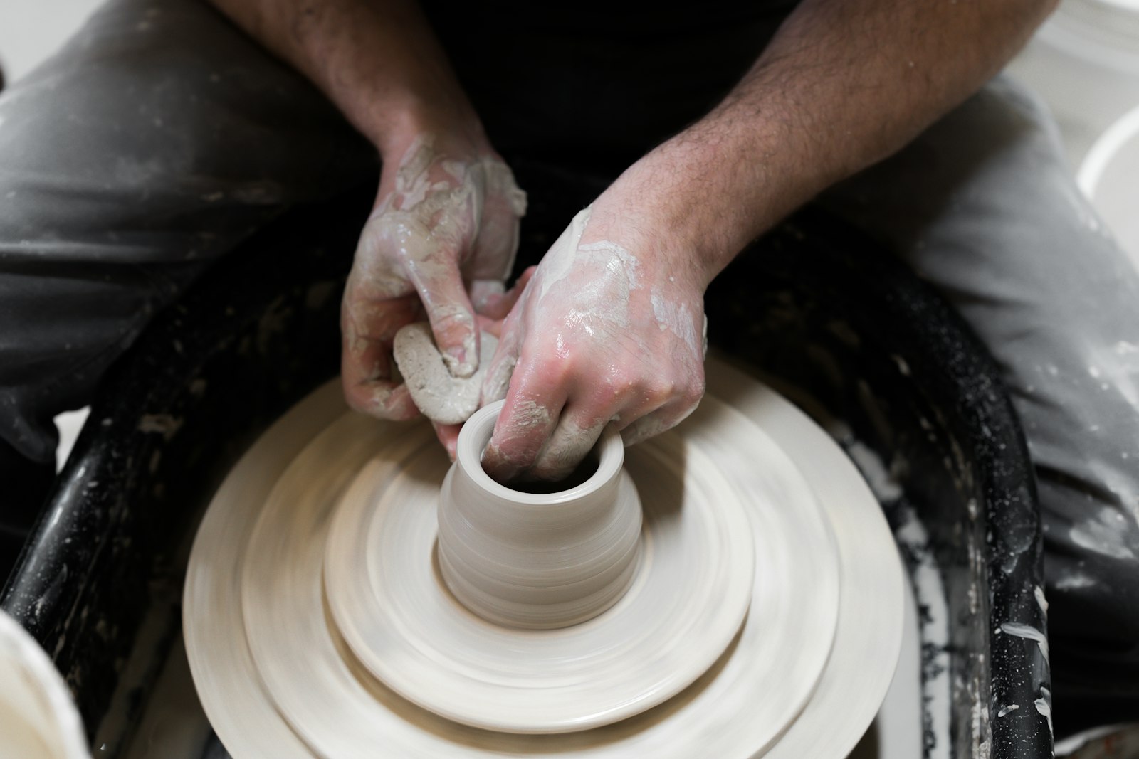 A maker's hands centring pale clay on a spinning pottery wheel