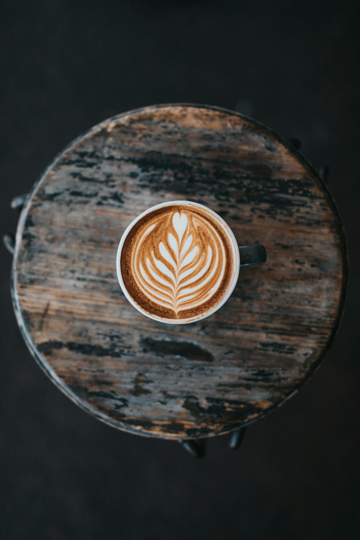 Rosetta latte art in a white cup on a worn timber stool