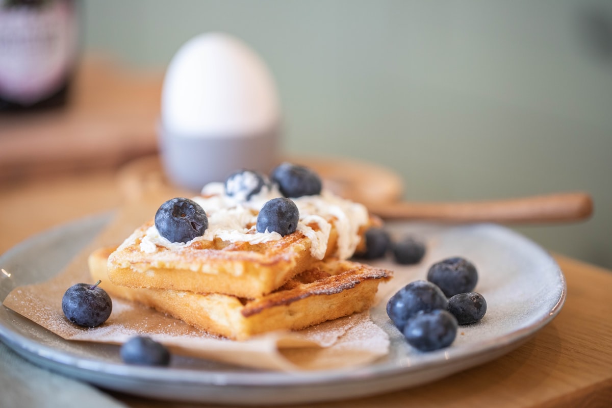 Waffles with blueberries and cream against a sage green wall