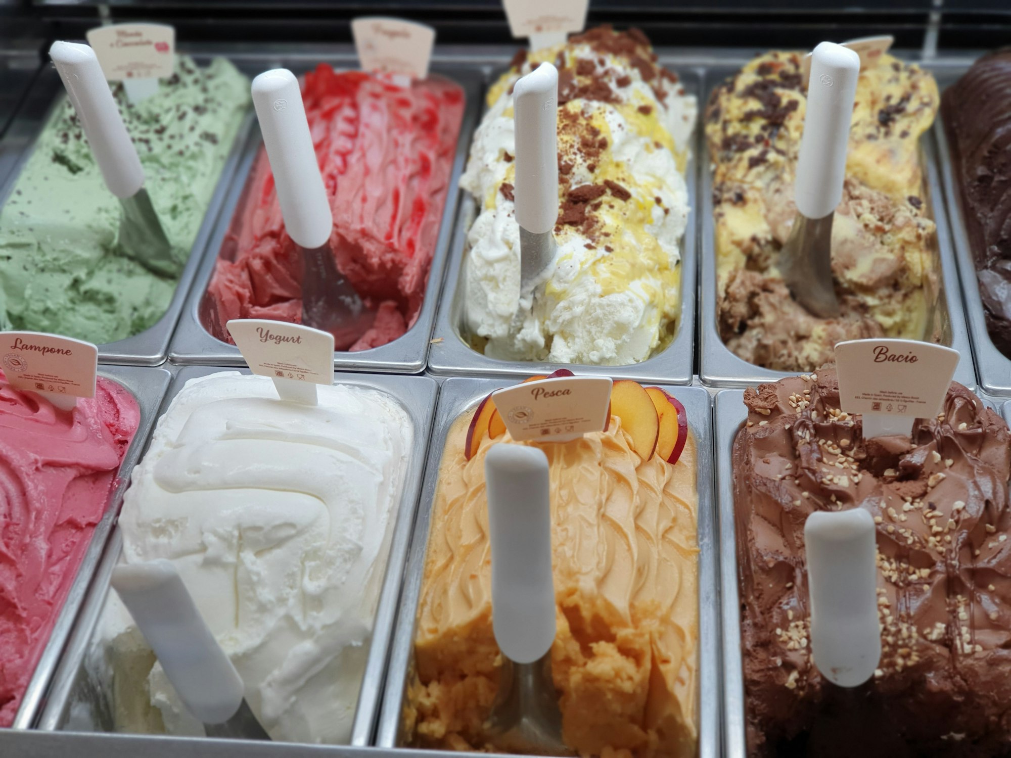 Gelato cabinet filled with colourful trays of pistachio, strawberry, peach and chocolate gelato