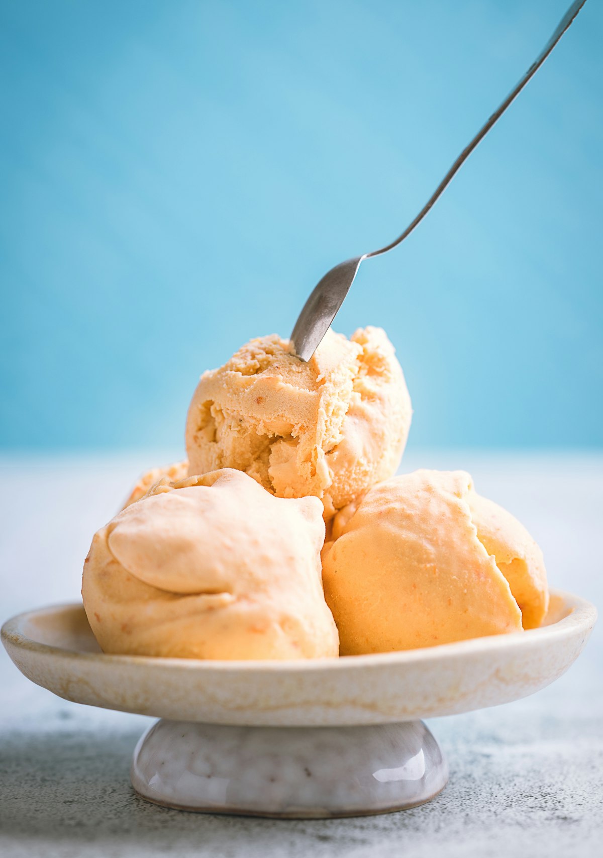 Peach gelato scoops in a ceramic dish on a blue background