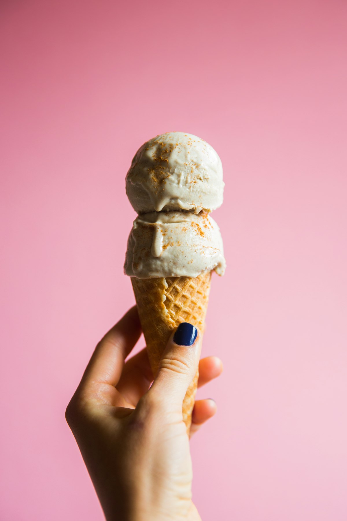 Cinnamon-dusted double scoop cone against a pink wall